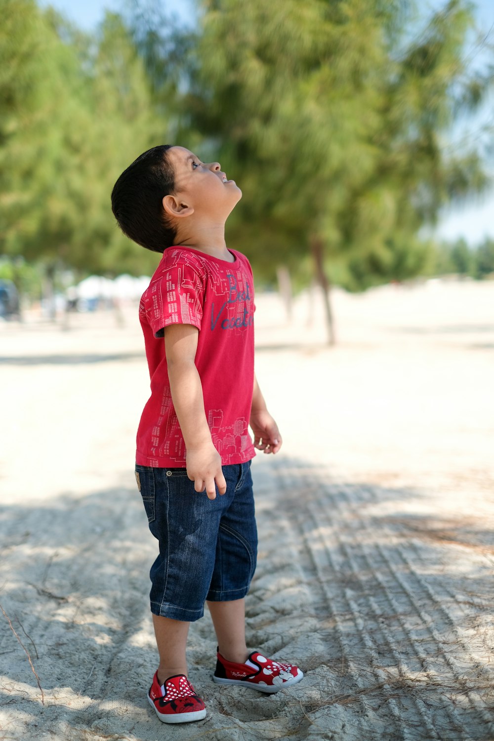 girl in red shirt and blue denim jeans standing on gray concrete road during daytime