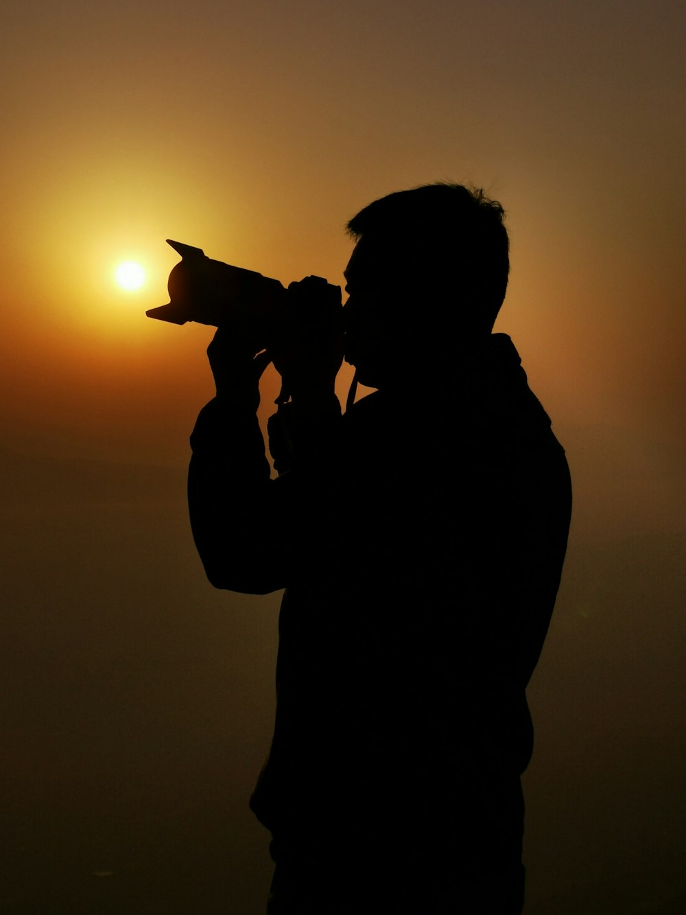silhouette of man holding camera during sunset