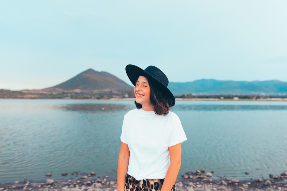 흰색 티셔츠와 검은 모자를 쓴 여자가 낮 동안 바위 해안에 서 있다