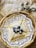 A woven basket holds an elegantly folded crepe dusted with powdered sugar and garnished with fresh blueberries. The crepe rests on a decorative white lace paper. In the background, ornate salt and pepper shakers are placed on a beige cloth napkin.