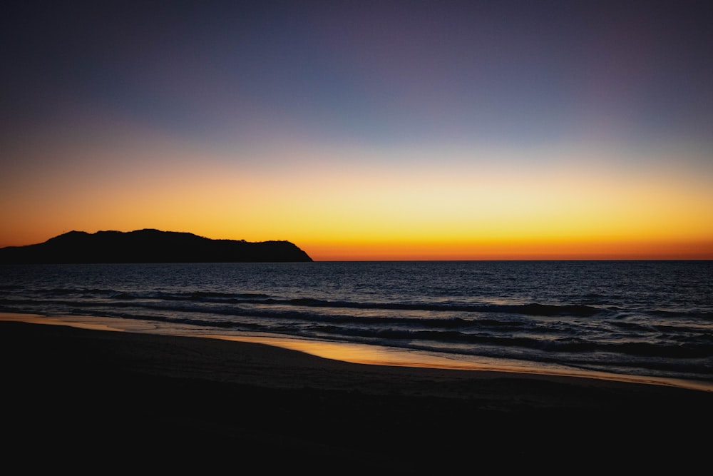 silhouette of mountain beside body of water during sunset