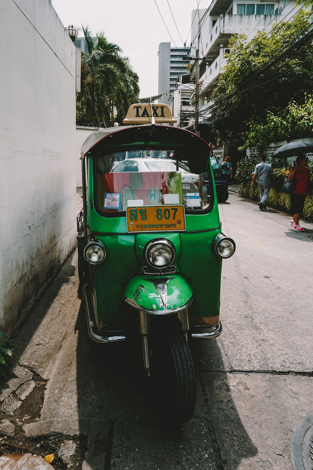 green and yellow auto rickshaw parked beside white concrete building during daytime