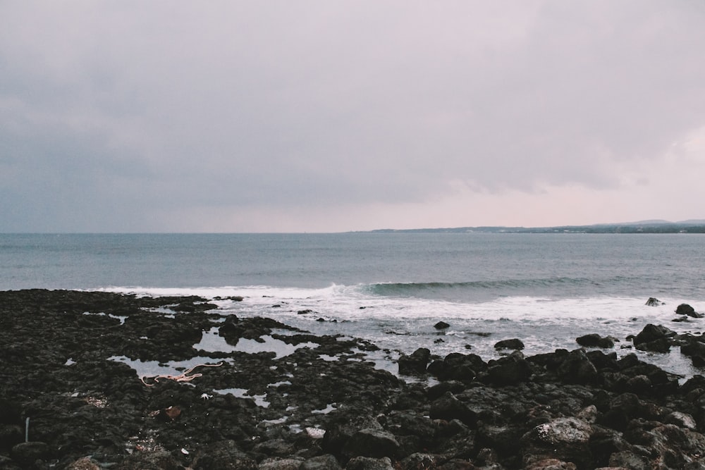 ocean waves crashing on rocks under white sky during daytime