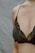 A close-up of a person wearing an elegant, lace-patterned black bra. The skin is softly lit, and the delicate necklace adds a touch of sophistication.