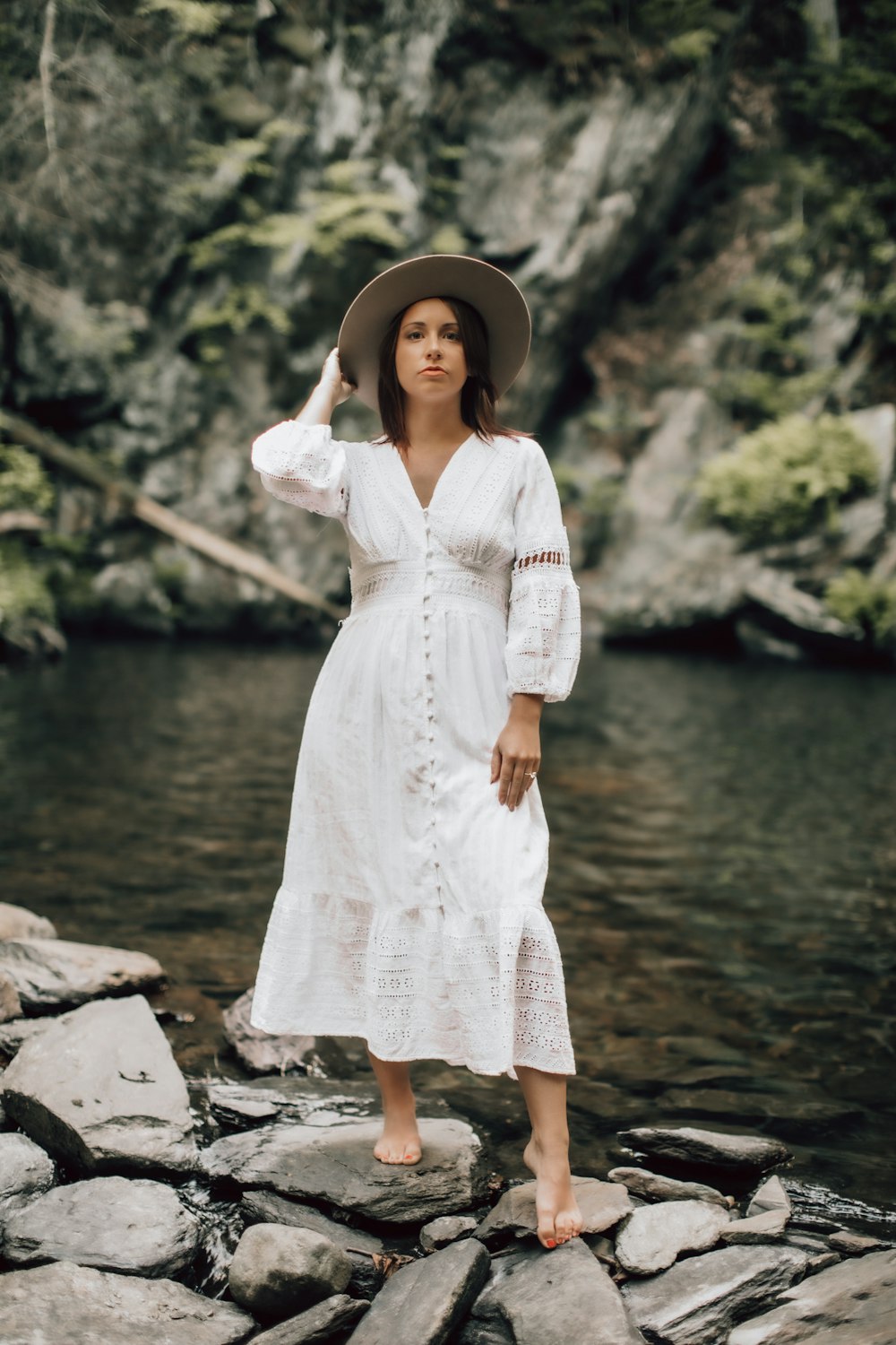 Frau im weißen Spitzenkleid tagsüber am felsigen Ufer stehend
