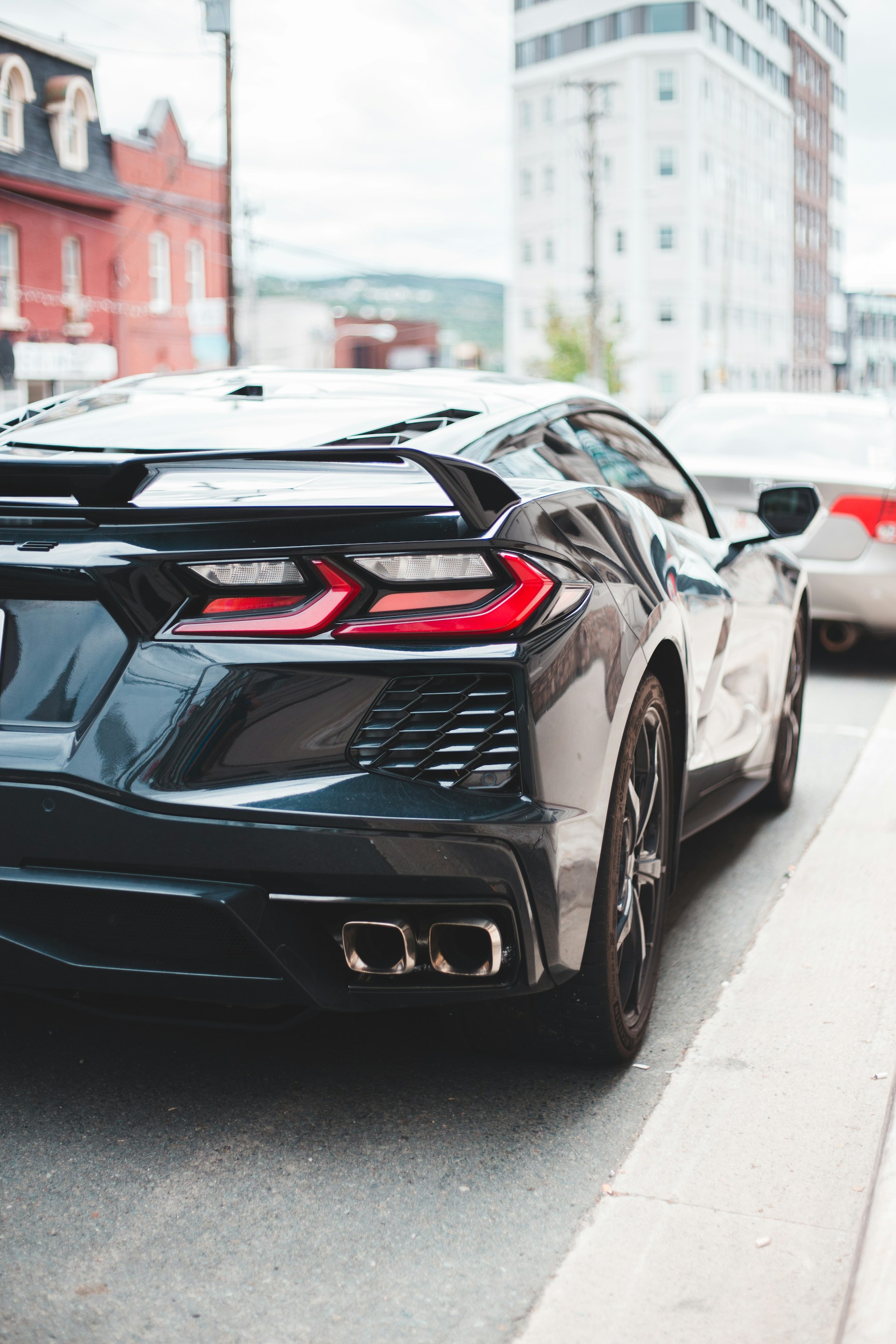 A sleek black luxury sports car parked on a sunlit city street, showcasing its polished curves and gleaming chrome details.