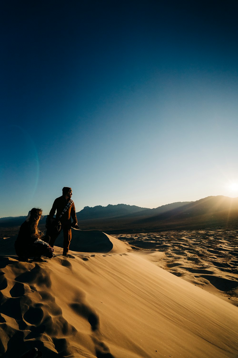 homme en veste noire et pantalon noir debout sur le sable brun pendant la journée