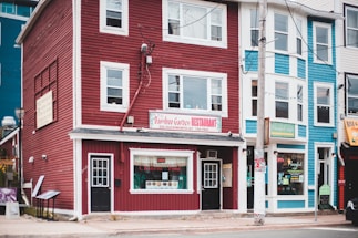 A street view featuring colorful buildings including a red building housing a restaurant with a sign for 'Bamboo Garden Restaurant' advertising Chinese food. The neighboring blue building also has a visible shop sign. The facade includes large windows and multiple stories.