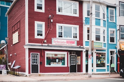 A street view featuring colorful buildings including a red building housing a restaurant with a sign for 'Bamboo Garden Restaurant' advertising Chinese food. The neighboring blue building also has a visible shop sign. The facade includes large windows and multiple stories.