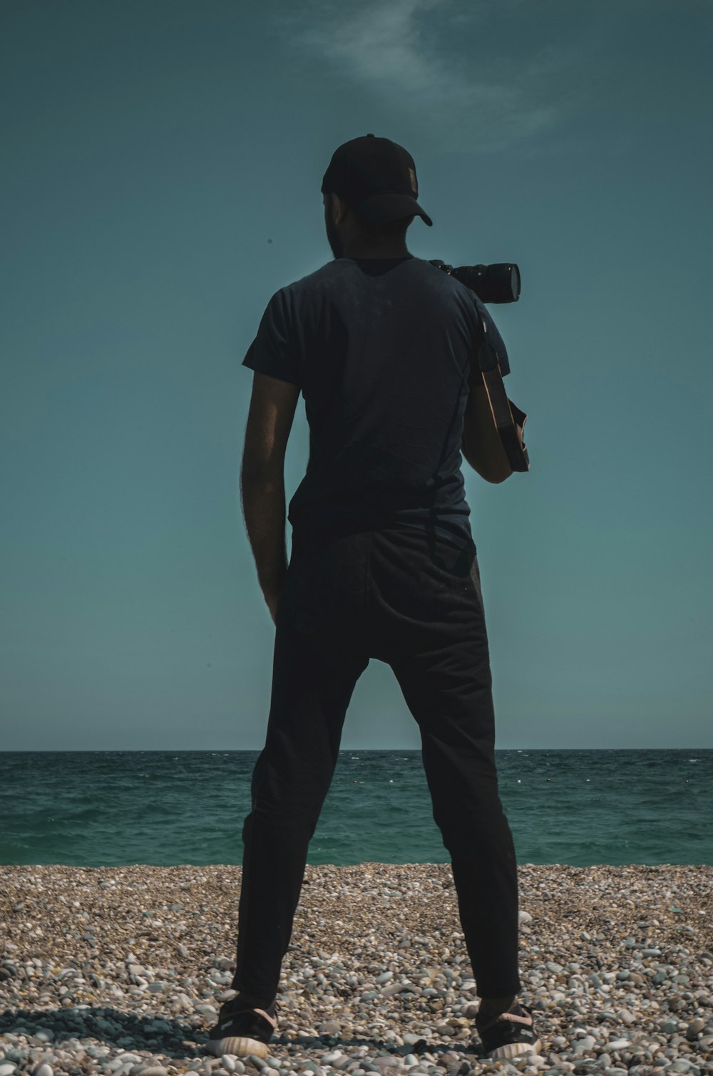 man in black t-shirt and black pants holding black dslr camera standing on beach during