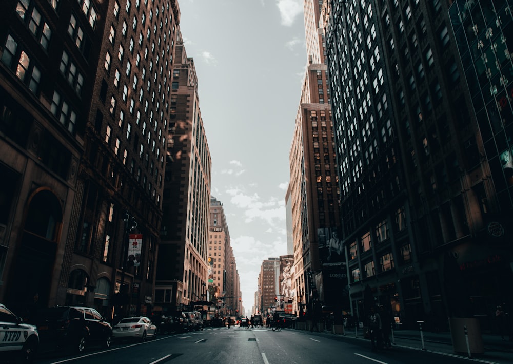 cars parked on side of the road in between high rise buildings during daytime