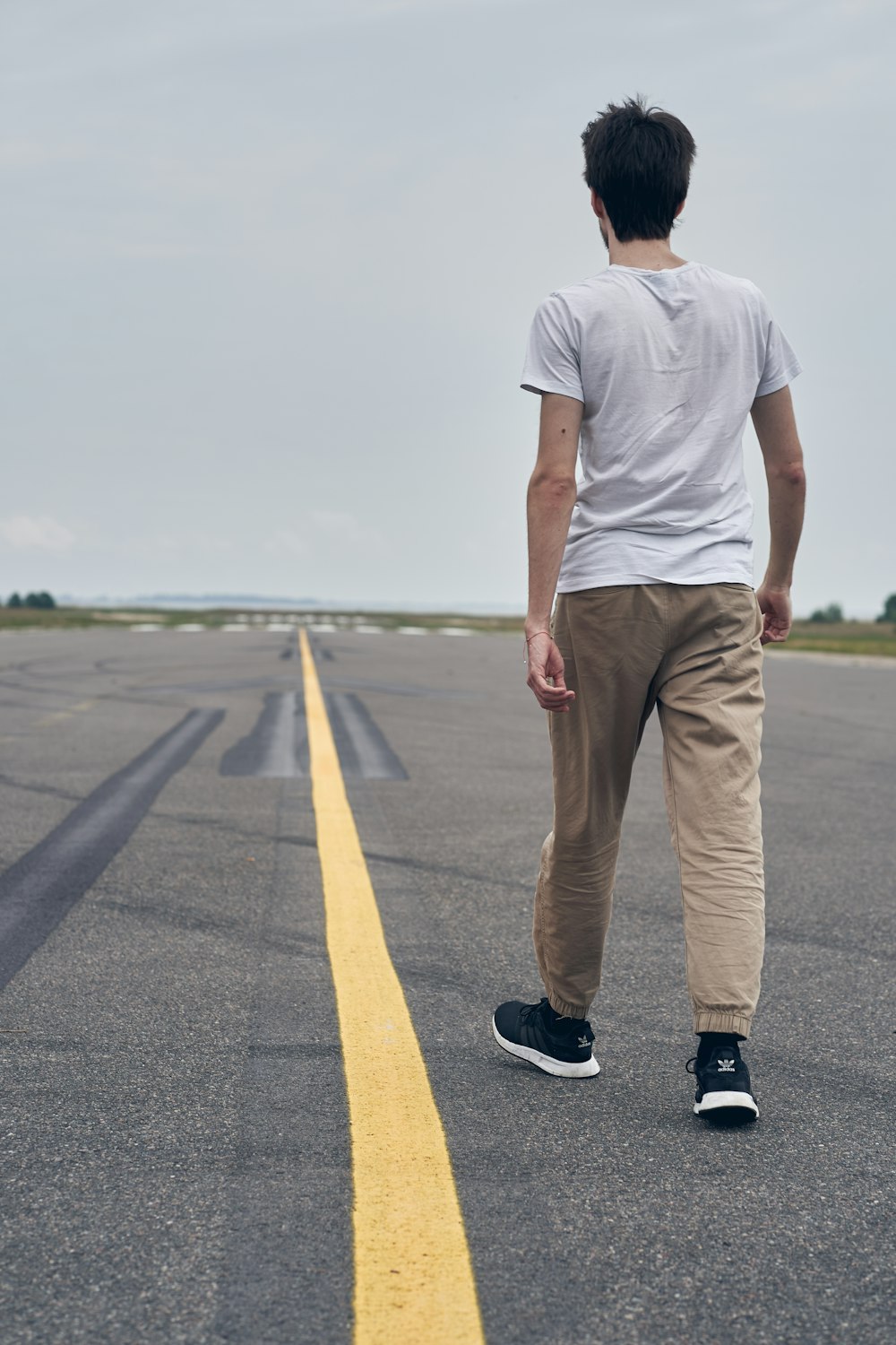 흰색 티셔츠와 갈색 바지를 입은 남자가 낮에 도로에 서 있다