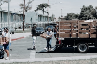 man in black jacket and blue denim jeans standing beside brown wooden box trailer during daytime