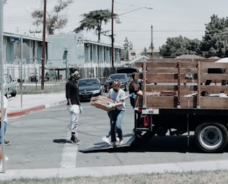 man in black jacket and blue denim jeans standing beside brown wooden box trailer during daytime