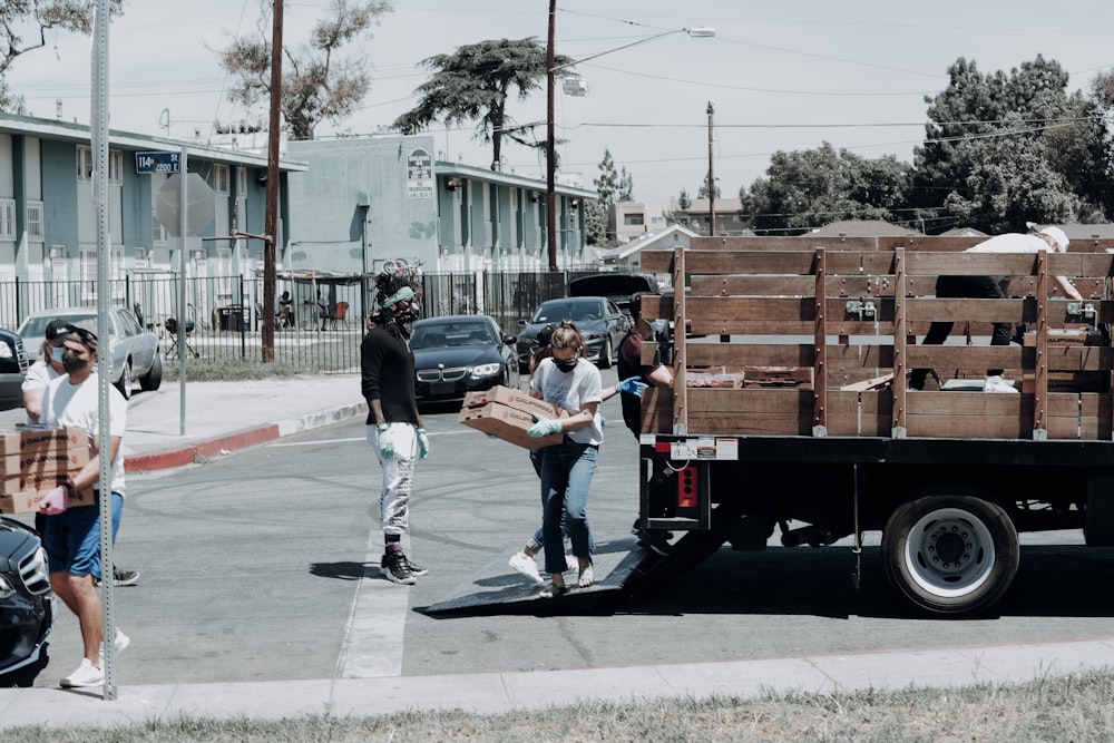 Hombre con chaqueta negra y jeans de mezclilla azul de pie junto a un remolque de caja de madera marrón durante el día