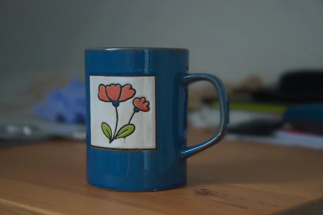 Close-up of a vibrant blue ceramic mug with a heart-shaped handle resting on a wooden table.