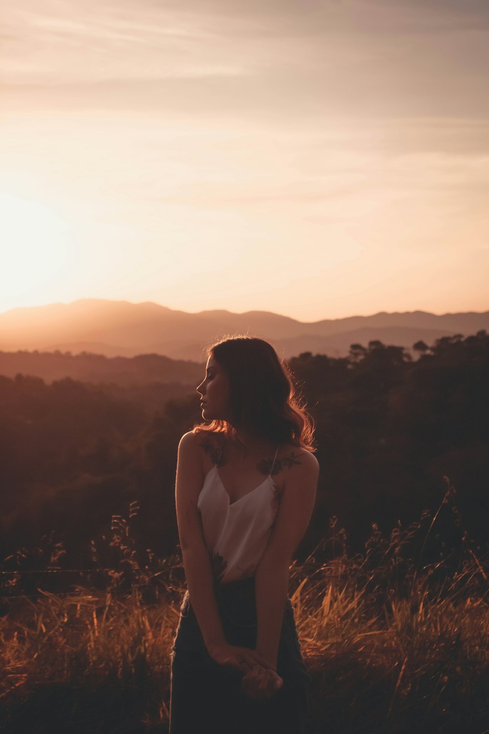 woman in white tank top sitting on brown grass during sunset