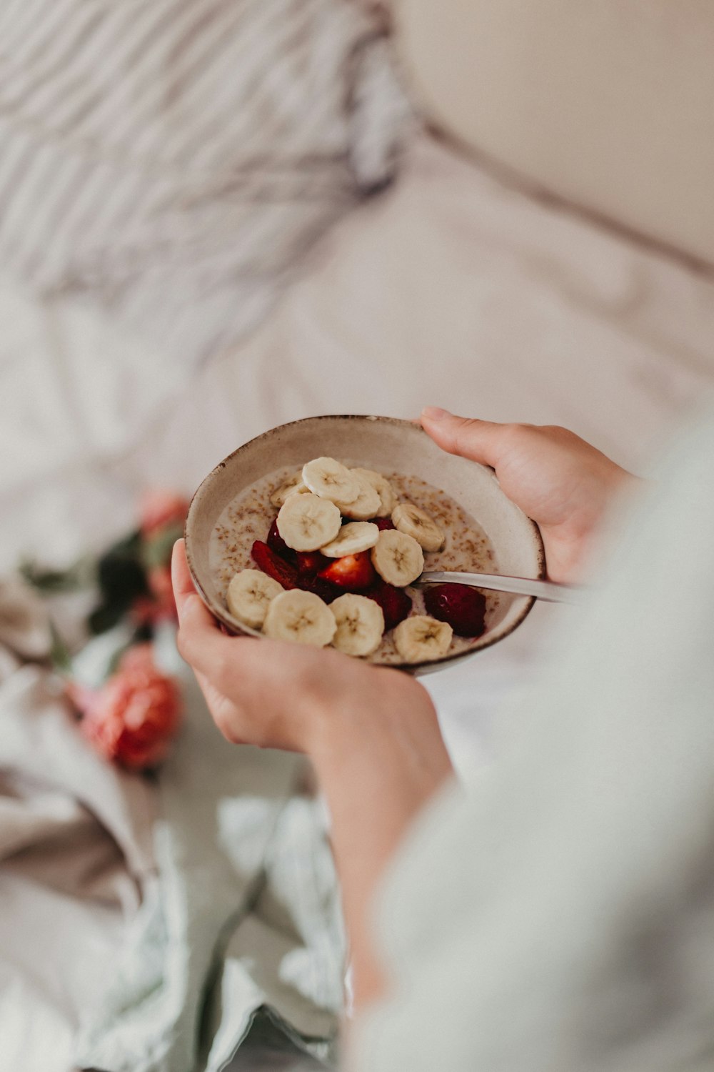 person holding stainless steel spoon and round brown bowl with food