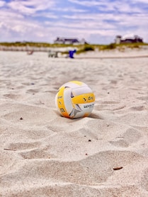 yellow and white volleyball on white sand during daytime