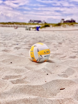 yellow and white volleyball on white sand during daytime