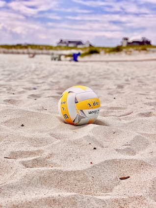 yellow and white volleyball on white sand during daytime