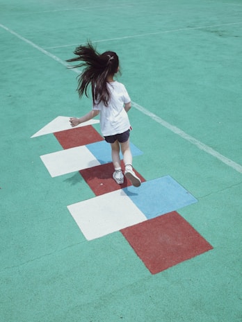 A school playground scene from the 1970s with children playing hopscotch and wearing colorful jackets.