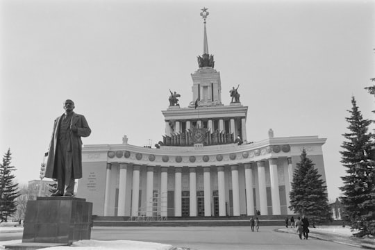man in black coat standing near white building in All-Russia Exhibition Centre Russia