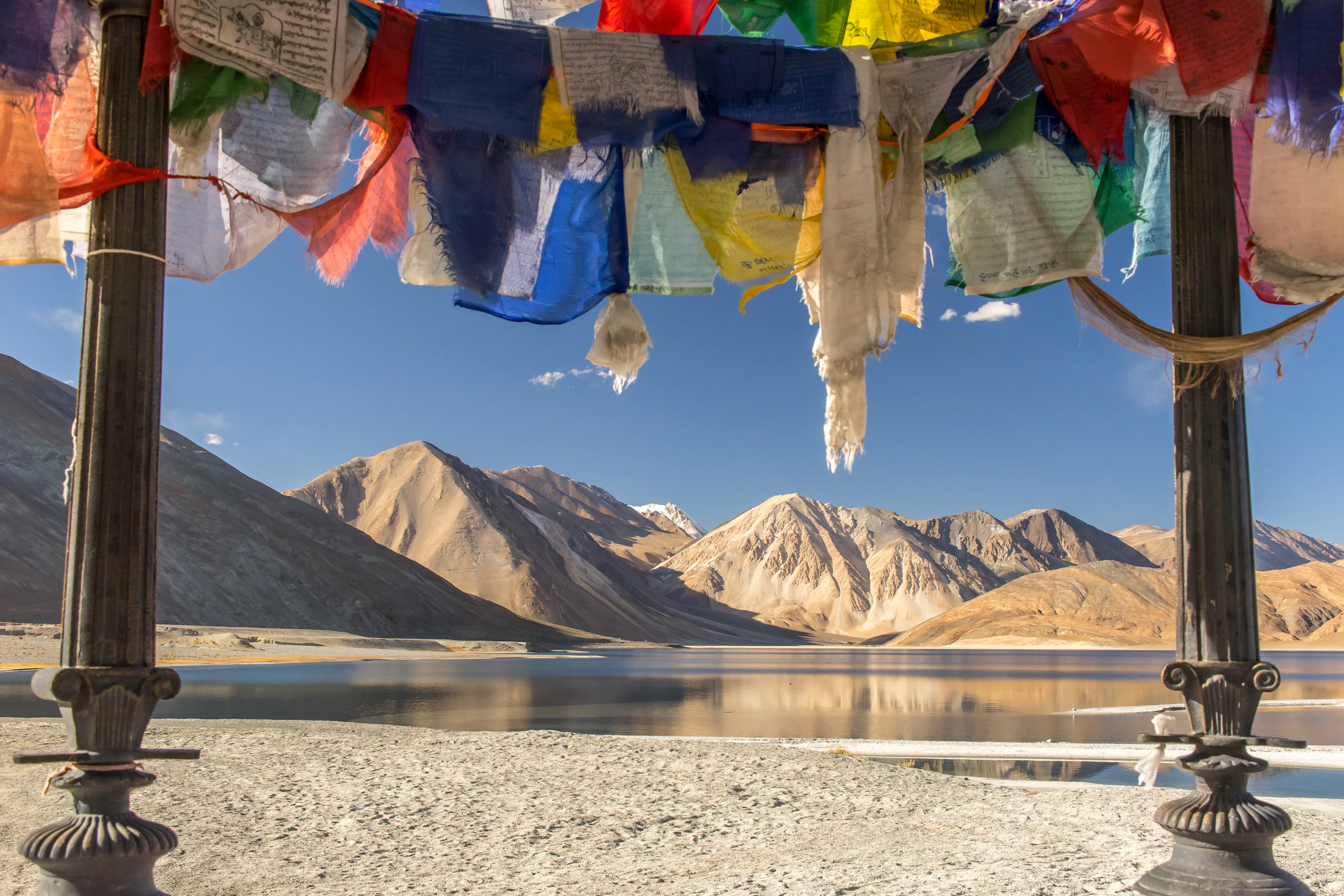 Prayer flags beside the blue waters of a Ladakh lake with bare mountains