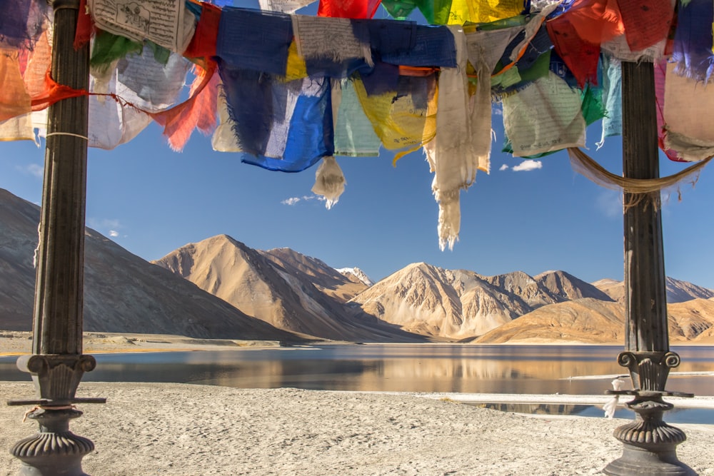 blau-gelbes und rotes Textil auf grauem Sand in der Nähe von See und Berg tagsüber