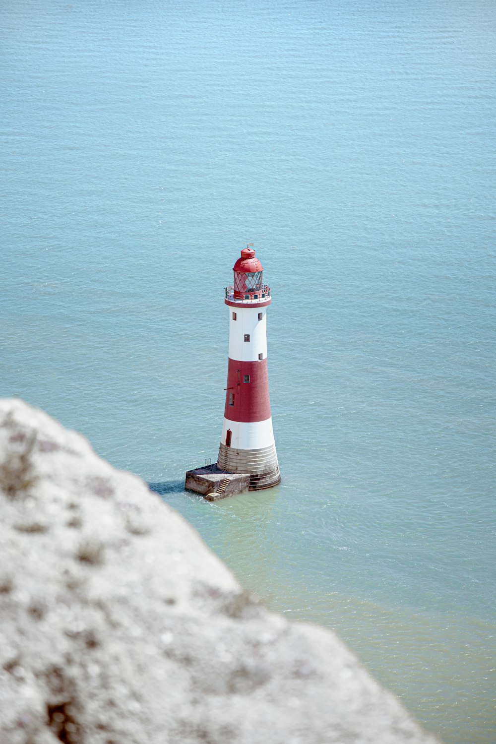 Faro bianco e rosso sulla formazione rocciosa accanto allo specchio d'acqua durante il giorno