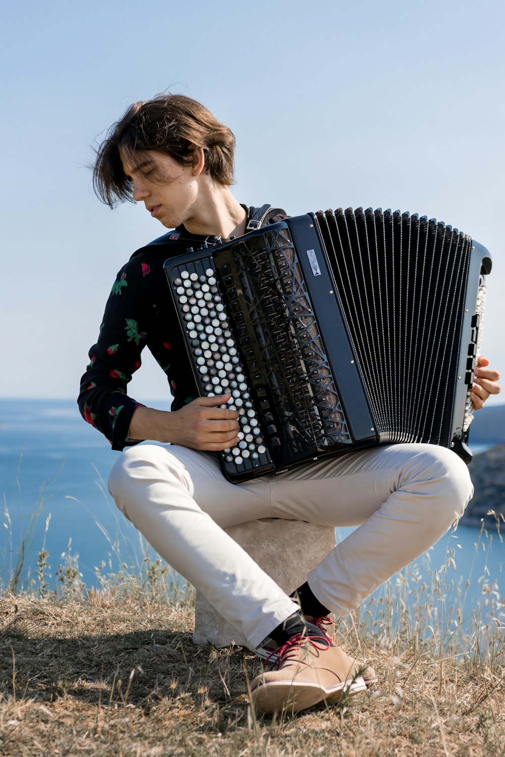 woman in green long sleeve shirt and white pants holding black and white accordion