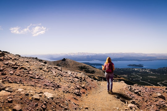 woman in red jacket standing on brown rocky hill during daytime in Parque Nacional Nahuel Huapi Argentina