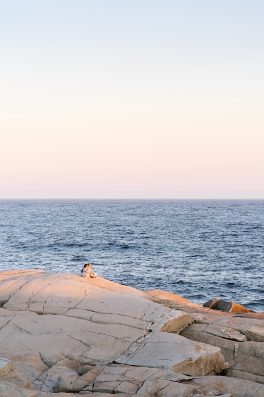 person sitting on brown rock near body of water during daytime in Peggys Cove Canada
