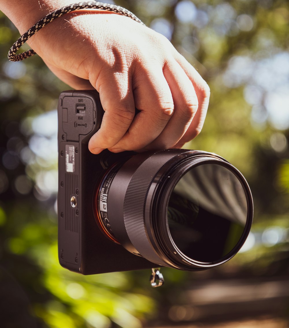 person holding black point and shoot camera