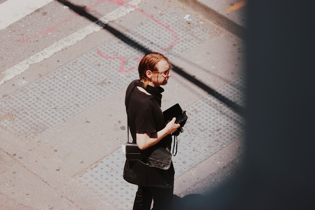 woman in black jacket holding camera standing on sidewalk during daytime