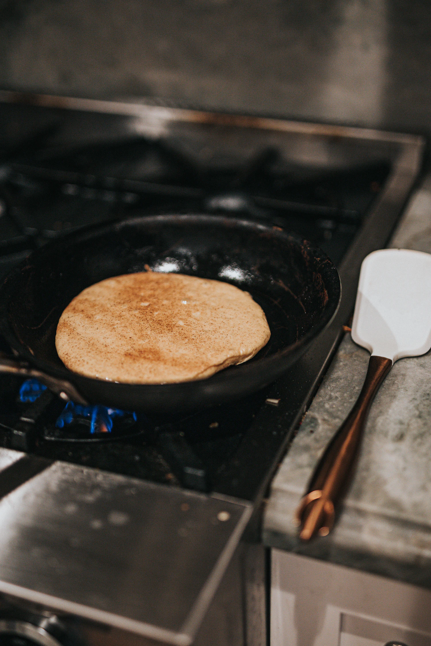 A round flatbread cooking in a black pan on a hob, a spatula resting beside it