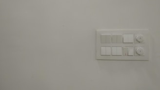 A plain white wall featuring a rectangular panel on the right side with several electrical switches and two rotary knobs.
