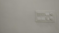 A plain white wall featuring a rectangular panel on the right side with several electrical switches and two rotary knobs.
