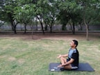 A person meditating outdoors at sunrise with a digital tablet beside them.