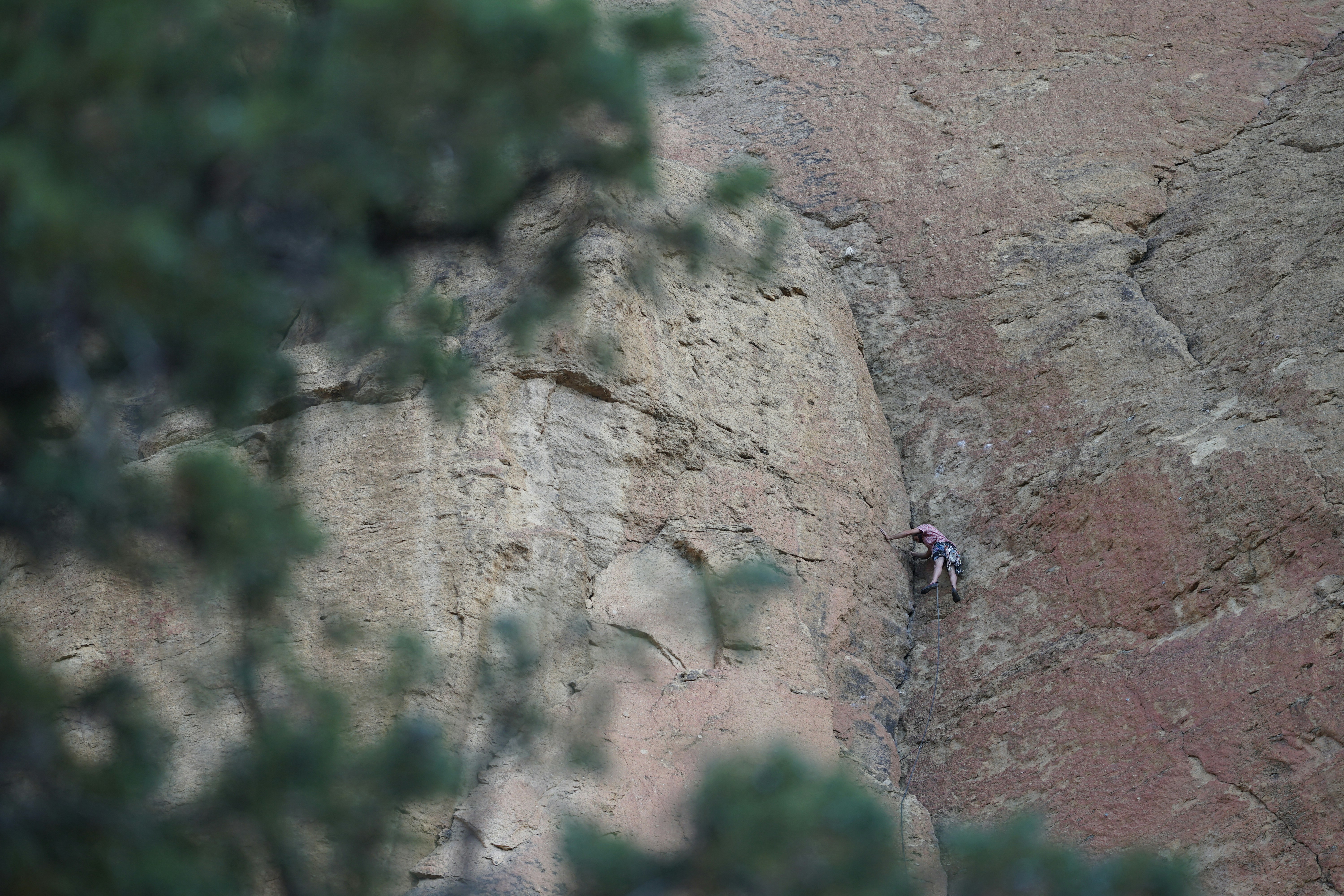 Rock climber scaling a steep cliff face with mountain views below