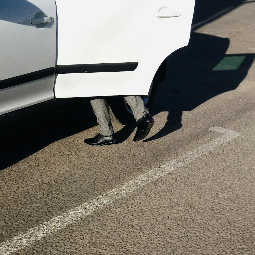 person in black shoes standing beside white car