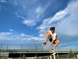 An energetic action shot of a skateboarder mid-trick against a clear blue sky.