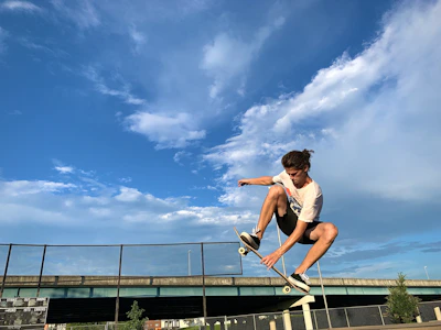 An energetic action shot of a skateboarder mid-trick against a clear blue sky.