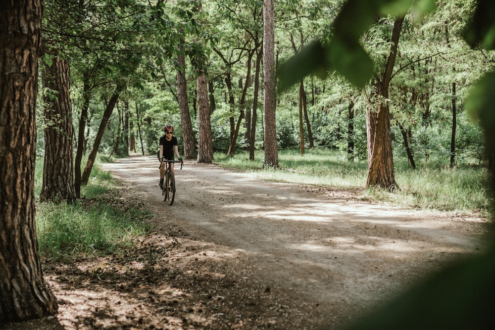 Hombre en chaqueta negra montando en bicicleta en camino de tierra entre árboles verdes durante el día