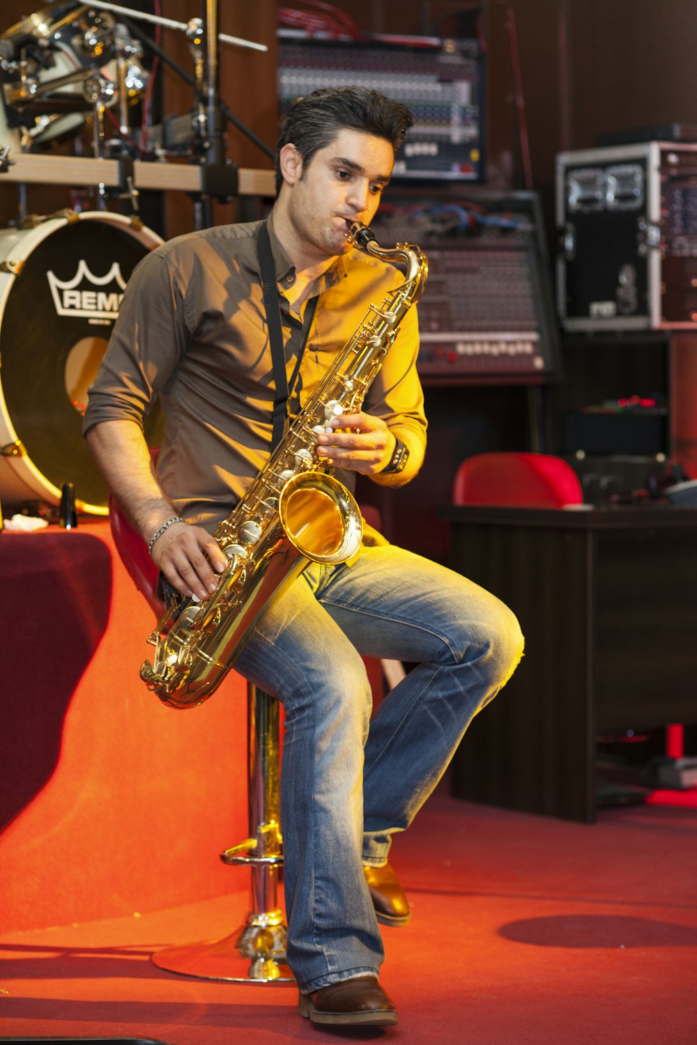 man in black polo shirt and blue denim jeans playing saxophone