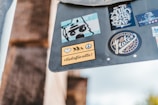A collection of colorful stickers is placed on a gray surface. Each sticker features different designs and logos, including a bear-like drawing, abstract text, and a peace symbol. One of the stickers displays the hashtag '#liebefüralle!' along with silhouettes of people running and a peace sign.