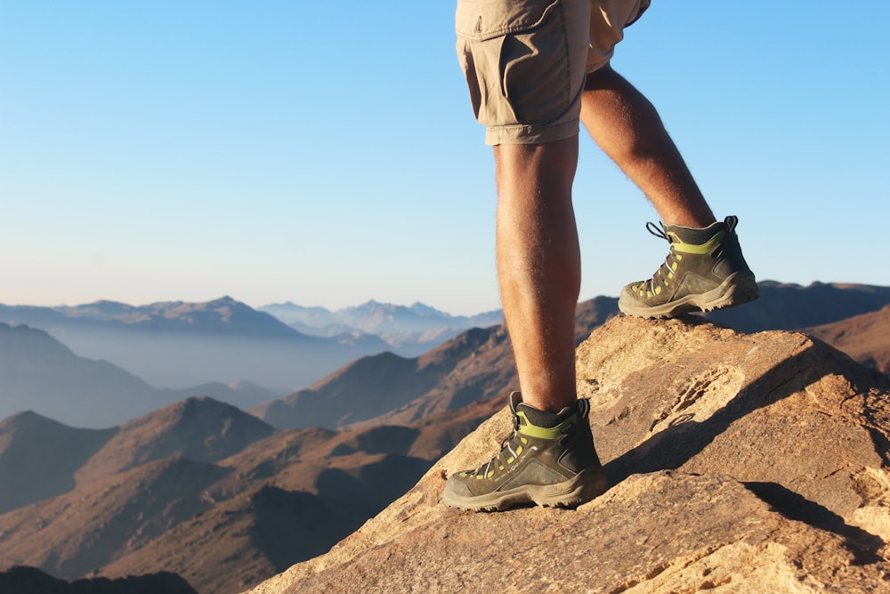 man in brown shorts and gray hiking shoes standing on brown rock mountain during daytime