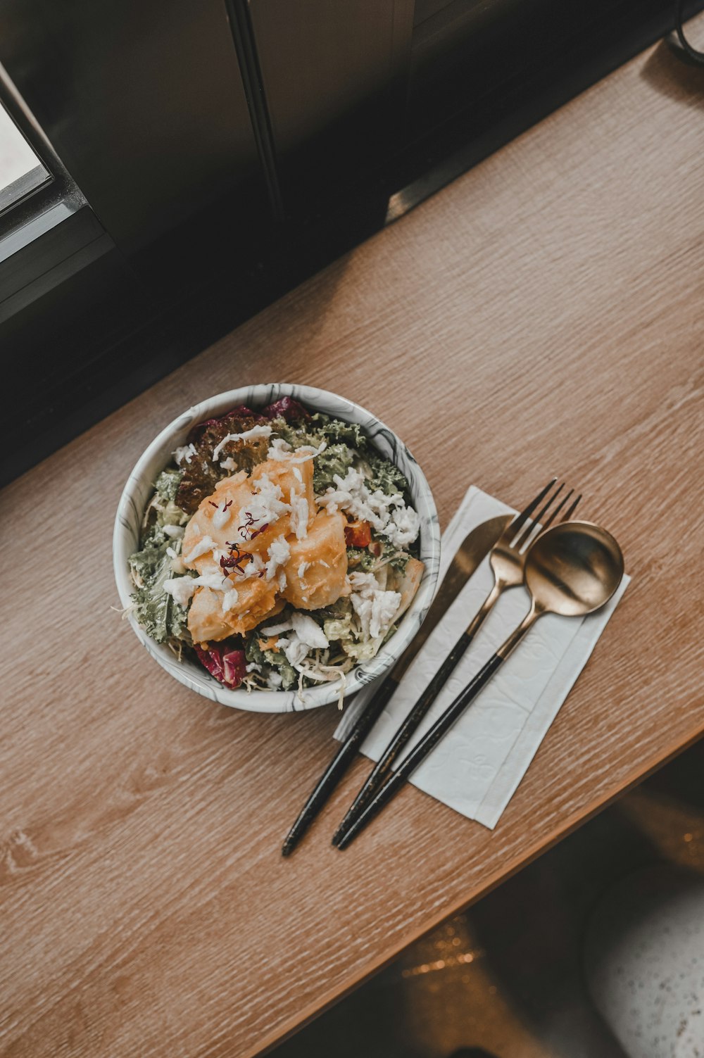 vegetable salad in white ceramic bowl beside stainless steel fork and knife on brown wooden table