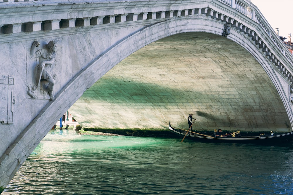 man in black shirt riding on boat on blue water under white concrete bridge during daytime