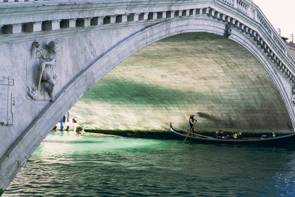 uomo in camicia nera che cavalca sulla barca sull'acqua blu sotto il ponte di cemento bianco durante il giorno